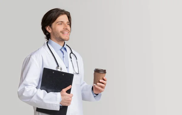 快乐的年轻医生拿着写有医疗信息的剪贴板，喝咖啡休息 — 图库照片