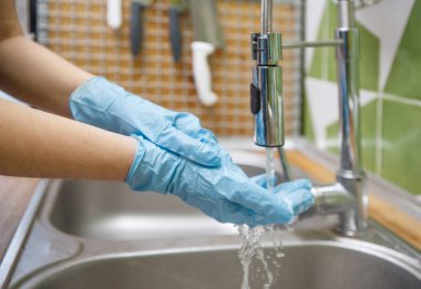 Eldivenli bir kadın mutfakta yemek yapmadan önce ellerini yıkıyor.