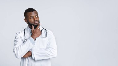 Beyaz üniformalı düşünceli siyah doktor fotokopi alanına bakıyor.