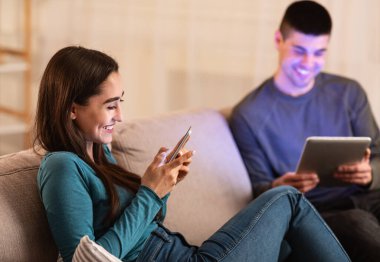 Çift koltukta oturup tablet ve akıllı telefon kullanıyor.