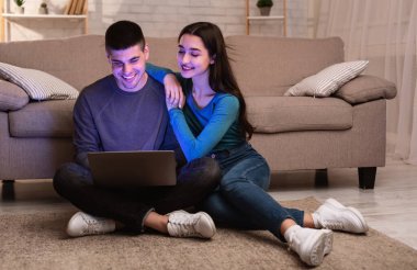 Mutlu çift yerde oturup bilgisayar kullanıyor.