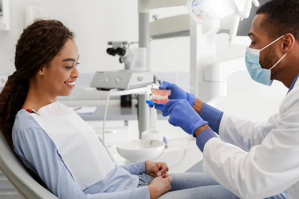 Siyah dişçi kadın hasta plastik çene gösteriyor. — Stok fotoğraf