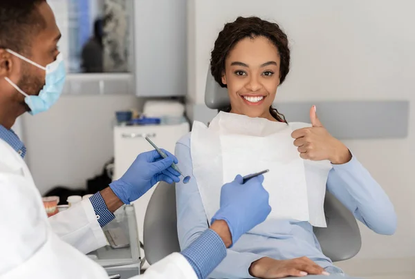 Mujer negra satisfecha mostrando pulgares hacia arriba en el gabinete del dentista — Foto de Stock