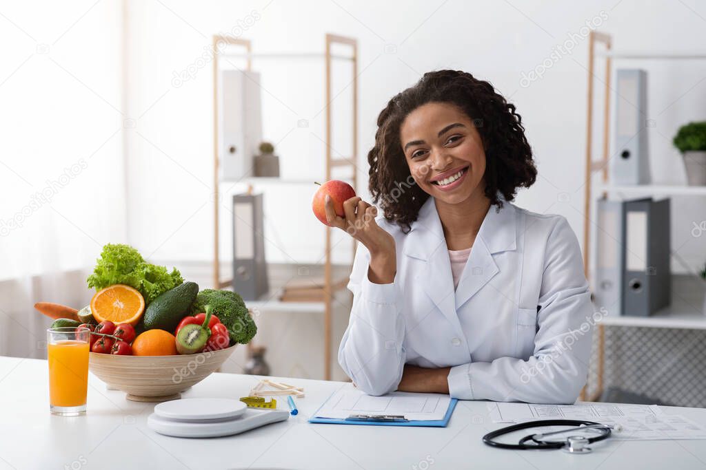 Beautiful cheerful female dietologist holding apple in her hand