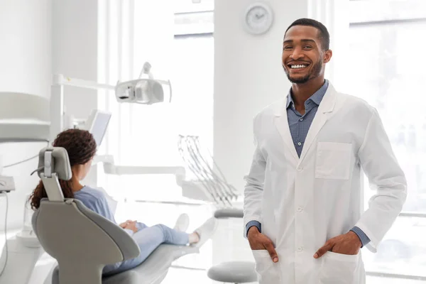 Koltukta oturan kadın hastanın yanında duran kendinden emin siyah dişçi. — Stok fotoğraf
