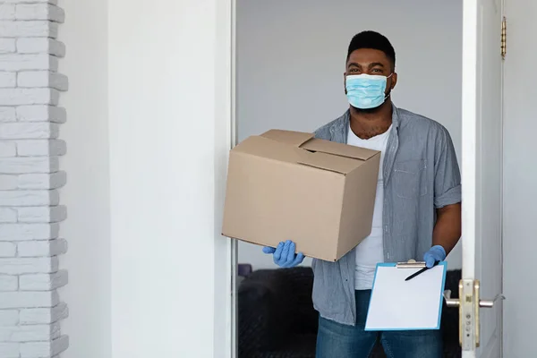 Livraison pendant le coronavirus. Courrier noir portant masque protecteur livré colis à la maison — Photo