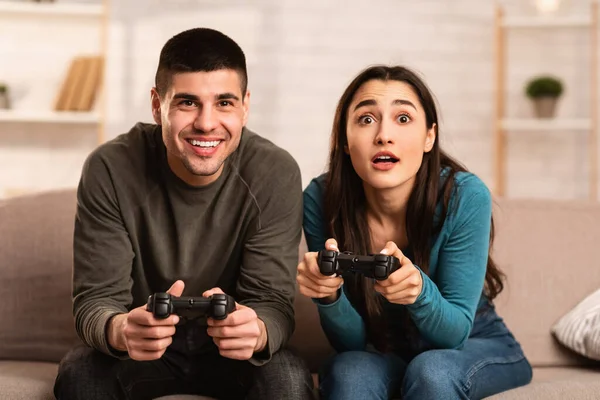 Νεαρό ζευγάρι κάθεται στον καναπέ παίζοντας βιντεοπαιχνίδια στο σπίτι — Φωτογραφία Αρχείου