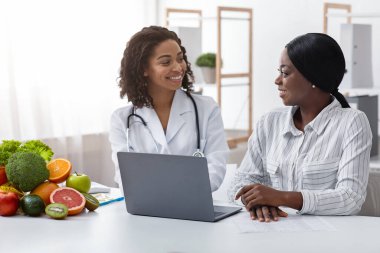 Klinikteki kadın hastayla gülümseyen siyah kadın doktor.