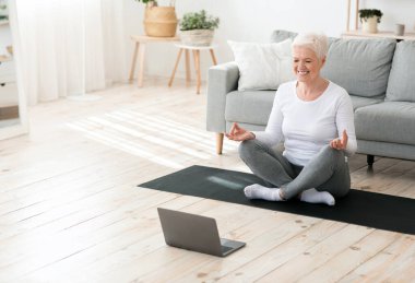 Yoga devrede. Evde laptopun önünde meditasyon yapan rahat bir yaşlı kadın.