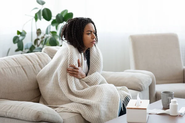 Sick black woman sitting on sofa covered with blanket, suffering from coronavirus — Stock Photo, Image