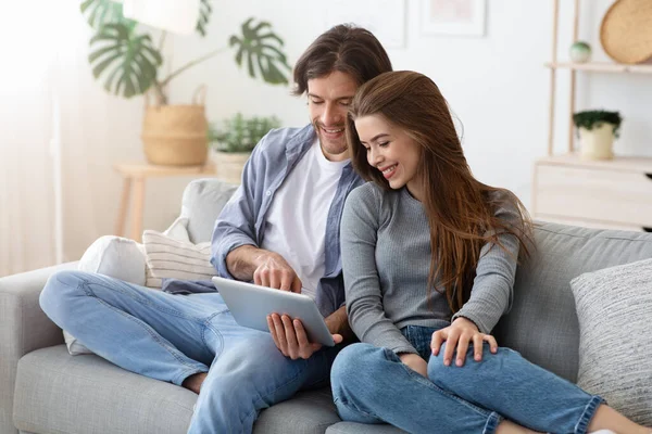 Hombre y mujer sentados en el sofá en casa, usando la tableta —  Fotos de Stock