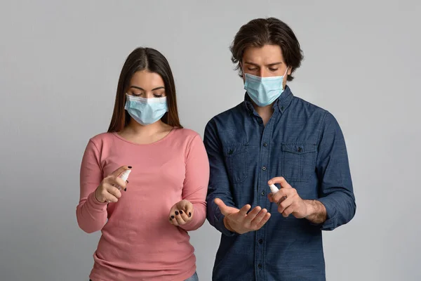 Άνδρας και γυναίκα με ιατρικές μάσκες που εφαρμόζουν απολυμαντικό σπρέι στα χέρια — Φωτογραφία Αρχείου