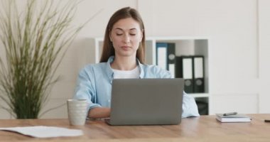 Laptopta çalışan ve kahve içen meşgul bir kadın.