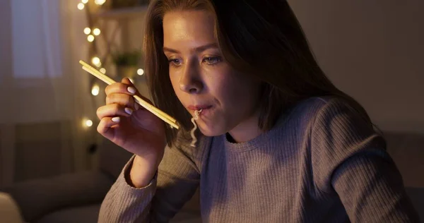 Mujer joven comiendo fideos chinos, viendo películas en el portátil — Foto de Stock