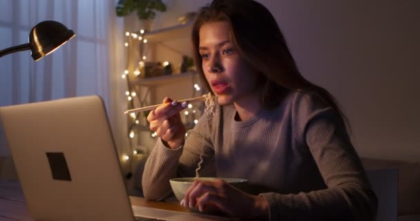 Молодая женщина ест китайскую еду, смотрит видео поздно на ноутбуке — стоковое видео