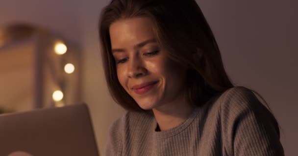 Молодая девушка болтает с друзьями в социальных сетях на ноутбуке поздно вечером — стоковое видео