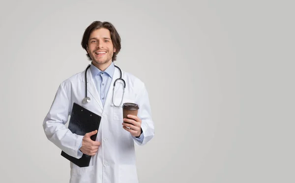 Retrato de un joven médico sonriente sosteniendo una carta médica y un café para llevar — Foto de Stock