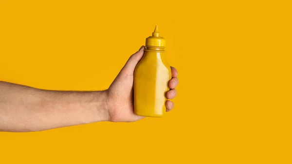 Nahaufnahme von Millennial-Kerl, der eine Quetschflasche Senf auf orangefarbenem Hintergrund zeigt, Design-Attrappe. Panorama — Stockfoto