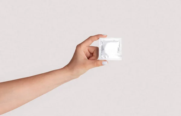 Bezpečný sex. Millennial dívka ukazuje kondom s obalem na světlém pozadí, detailní záběr ruky. Panorama — Stock fotografie