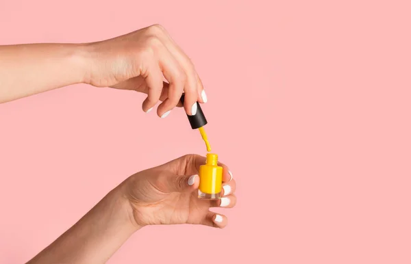 Close-up van nagel kunstenaar houden fles geel emaille op roze achtergrond, kopieer ruimte — Stockfoto