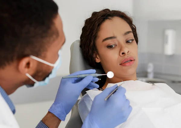 Налякана чорна жінка дивиться на зубні інструменти в руках лікаря — стокове фото