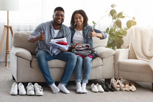 Jovem casal preto sentado ao lado dobrado roupas e sapatos em casa — Fotografia de Stock