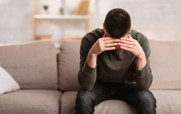 Worried man sitting on sofa with head on his hands