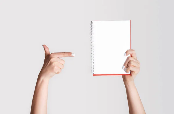 Kvinna pekar på tom anteckningsbok på ljus bakgrund, närbild. Mockup för design — Stockfoto