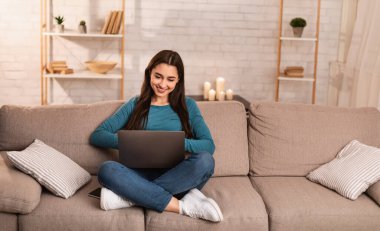 Kanepede oturan bir kadın bilgisayarını kullanıyor.