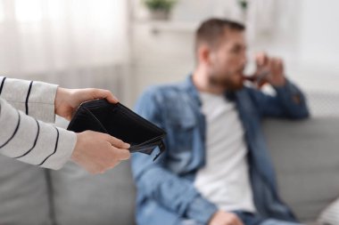 Boş cüzdan taşıyan bir kadın, arka planda alkolik bir adam.