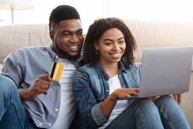 Siyah çift evde online alışveriş yapmak için laptop ve kredi kartı kullanıyor.