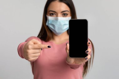 Tıbbi Maskeli Genç Kadın Siyah Ekranlı Akıllı Telefonu Gösteriyor