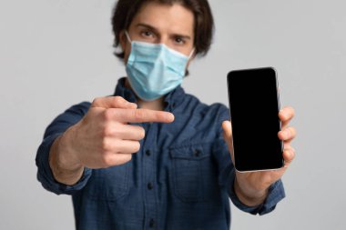 Cerrahi Maskeli Genç Adam Siyah Ekranlı Akıllı Telefonu Gösteriyor