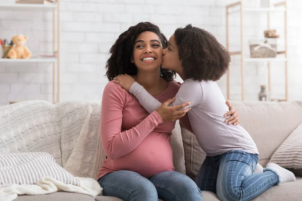 Lindo poco negro chica besos su feliz embarazada madre en casa — Foto de Stock