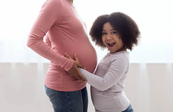 Izgatott kis fekete lány ölelkezik terhes hasát anyja — Stock Fotó