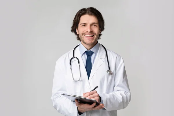 Orvosi vizsgálat. Barátságos fiatal doktor portréja írótáblával a kezében — Stock Fotó