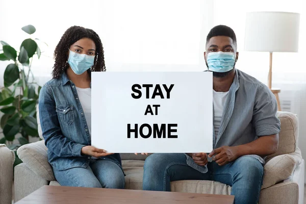 Stay At Home. African Couple Wearing Medical Masks And Holding Warning Placard