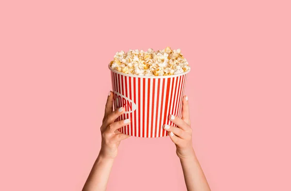 Ung flicka som håller randig hink med popcorn på rosa bakgrund, närbild — Stockfoto