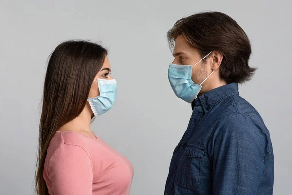Πορτρέτο του νεαρού ζεύγους σε προστατευτικές ιατρικές μάσκες κοιτάζοντας ο ένας τον άλλο — Φωτογραφία Αρχείου