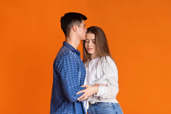 Хлопець цілує дівчину в чоло на оранжевому фоні. — стокове фото