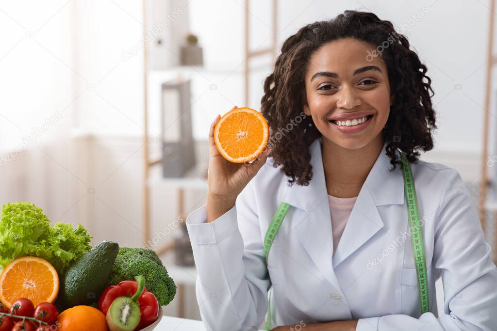 Cheerful female dietician holding fresh orange half