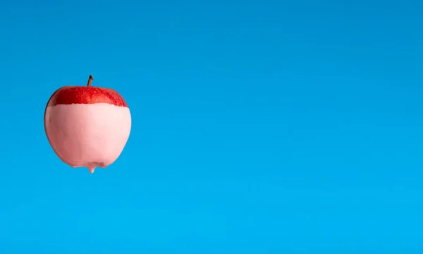 Pink paint dripping from red apple on blue background