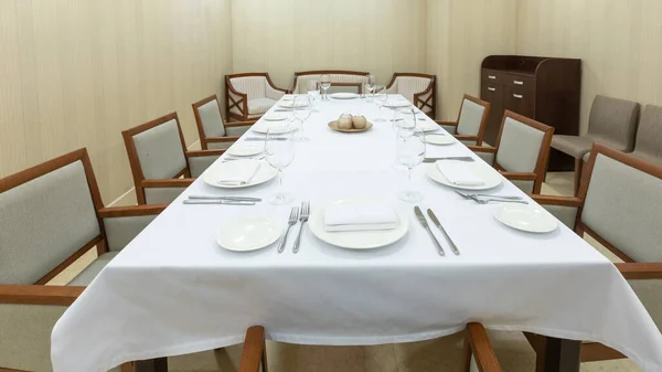 Big table with white tablecloth, plates and cutlery — Stock Photo, Image