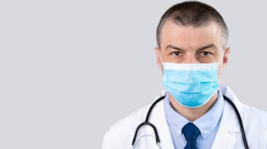 Maske takarak kameraya bakan olgun bir doktorun portresi.