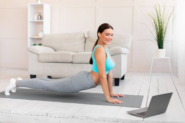 Kadın Laptop 'ta egzersiz yapıyor, geriniyor Evde Çevrimiçi Eğitimi İzliyor