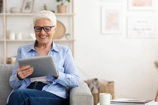 Uśmiechnięta starsza pani w okularach używająca tabletu cyfrowego w domu — Zdjęcie stockowe