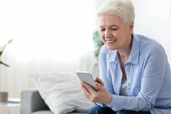 Domowy wypoczynek dla seniorów. Szczęśliwy starsza kobieta za pomocą smartfona w domu — Zdjęcie stockowe