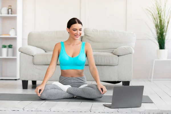 Adatto ragazza che pratica yoga al computer portatile che medita a casa — Foto Stock