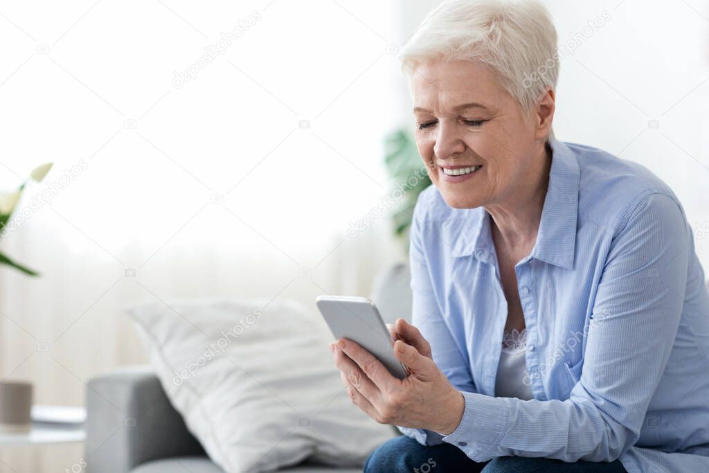 Home leisure for seniors. Happy elderly woman using smartphone at home