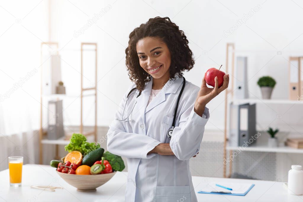 Positive female nutritionist posing at clinic, holding apple